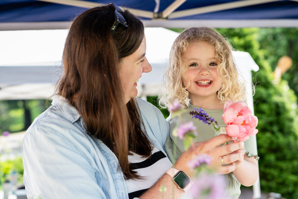 A young girl and a woman smile at each other as they hold flowers.