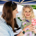 A young girl and a woman smile at each other as they hold flowers.