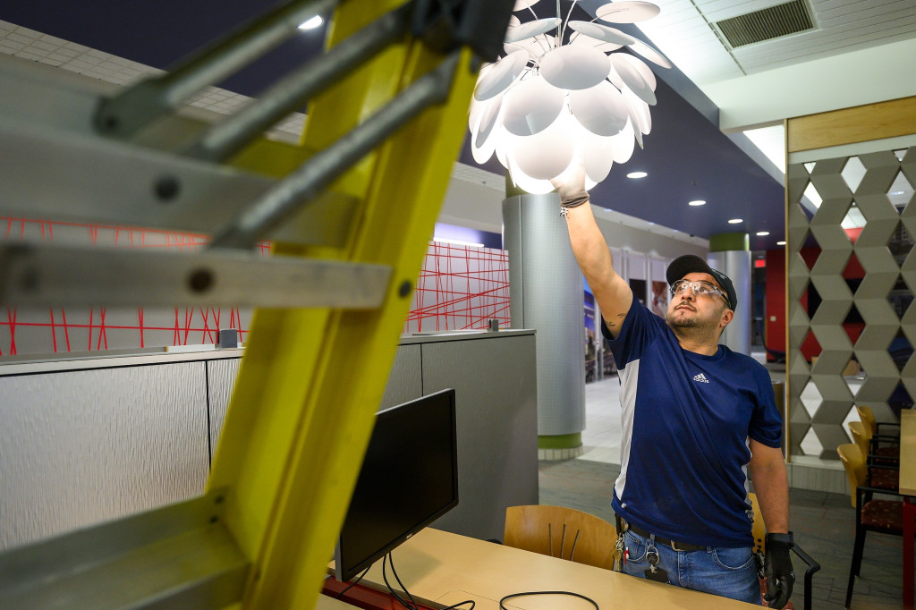 A man in a blue shirt unscrews a light bulb.