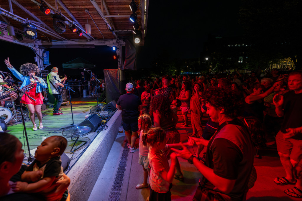 A crowd sitting on a terrace listens to a band on stage at night.