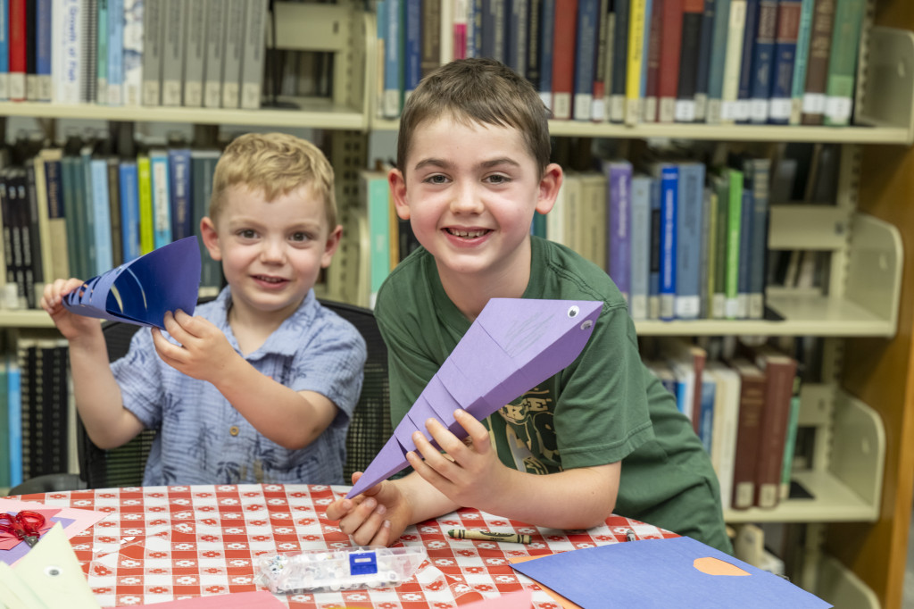 Two kids hold up paper masks they made.