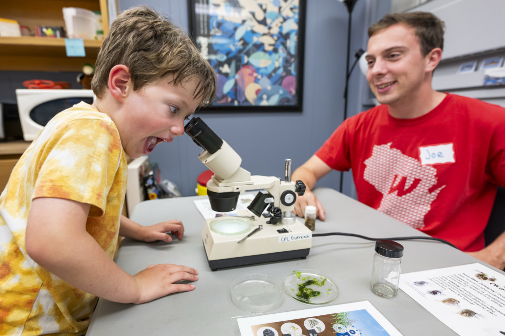 A young boy peers through a microscope and smiles and exclaims in delight.