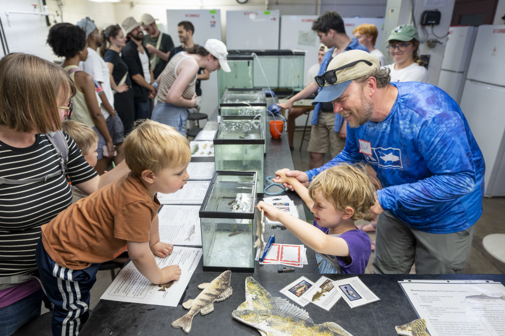 Adults and children gather around a table with fish tanks and paper fish cutouts on it.