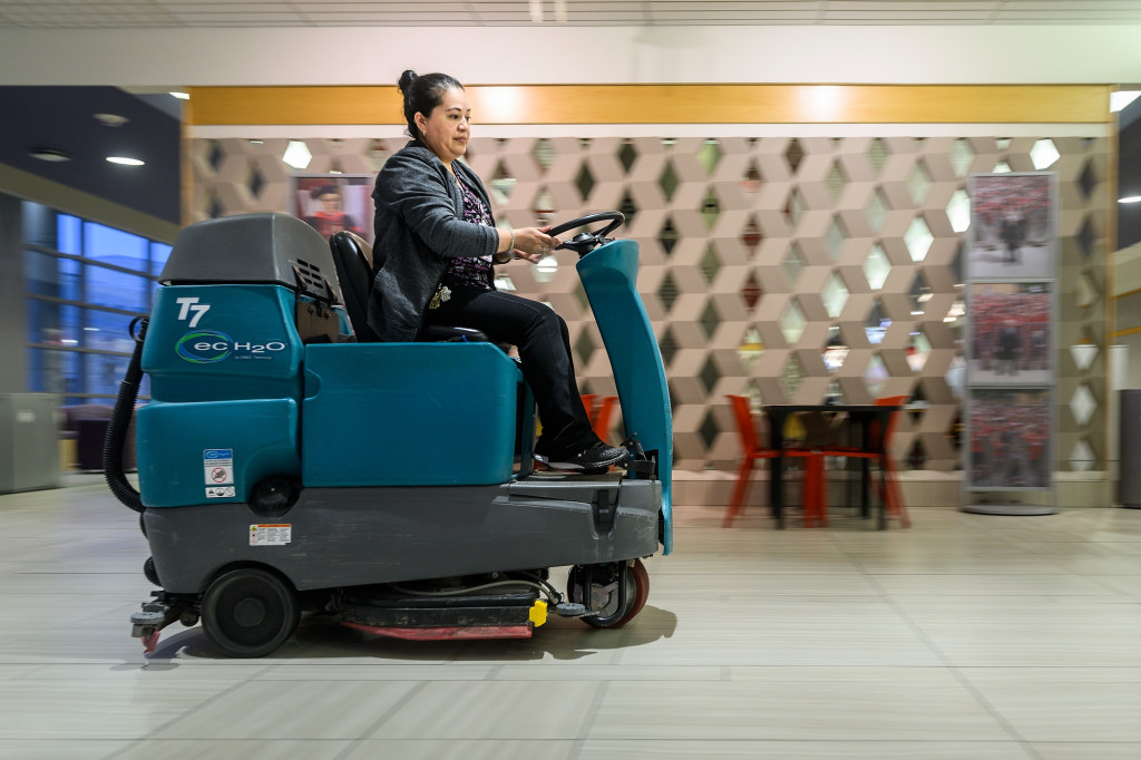 A woman rides a small vehicle that scrubs floors.