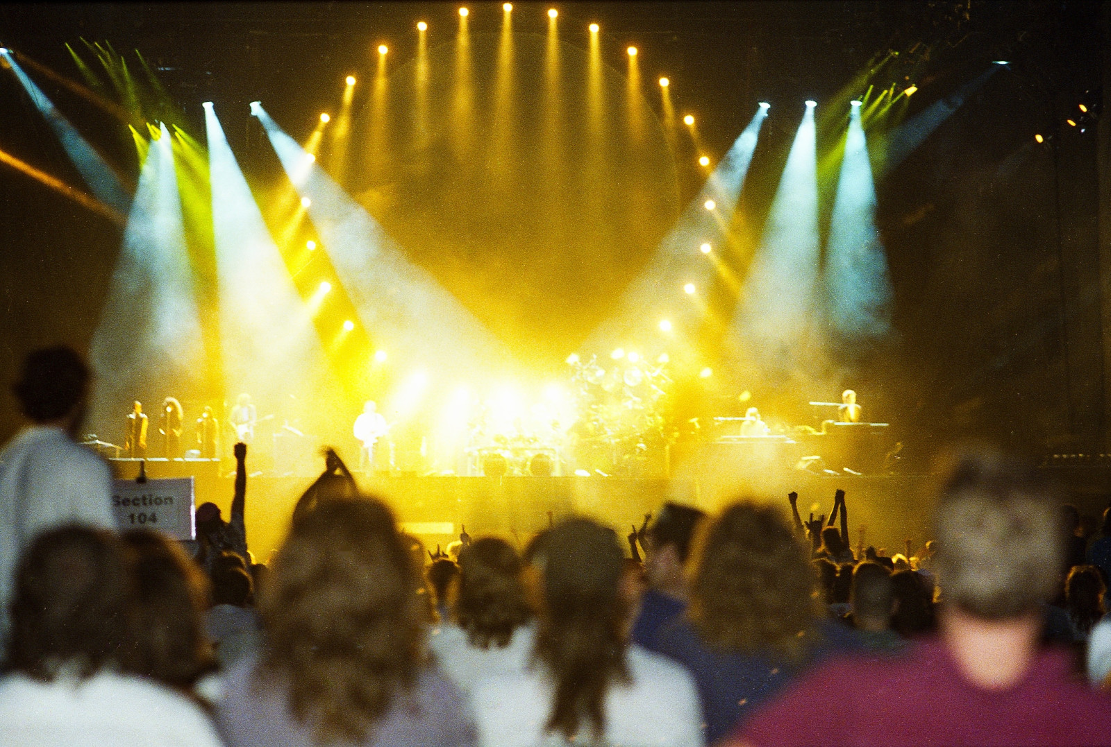 The front of a crowd looks toward the stage, where Pink Floyd band members are playing in front of bright spotlights.