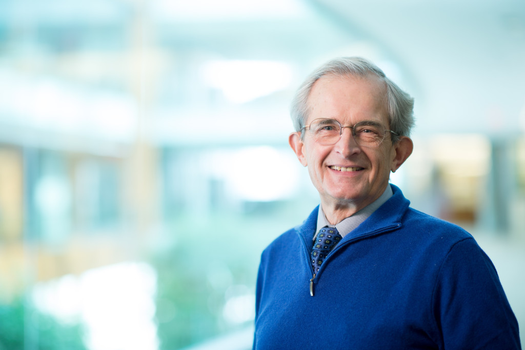 A man in a blue sweater and tie smiles at the camera.