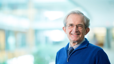 A man in a blue sweater and tie smiles at the camera.