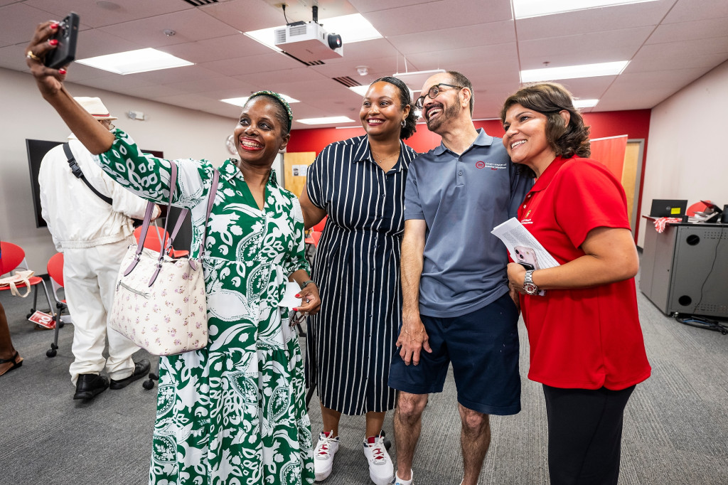 Rainey-Moore, Pearson, Lee and González stand in a line and smile for the cell phone camera being held up and in front of the group by Rainey-Moore.