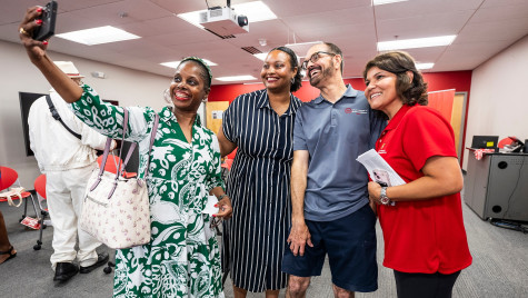 Rainey-Moore, Pearson, Lee and González stand in a line and smile for the cell phone camera being held up and in front of the group by Rainey-Moore.