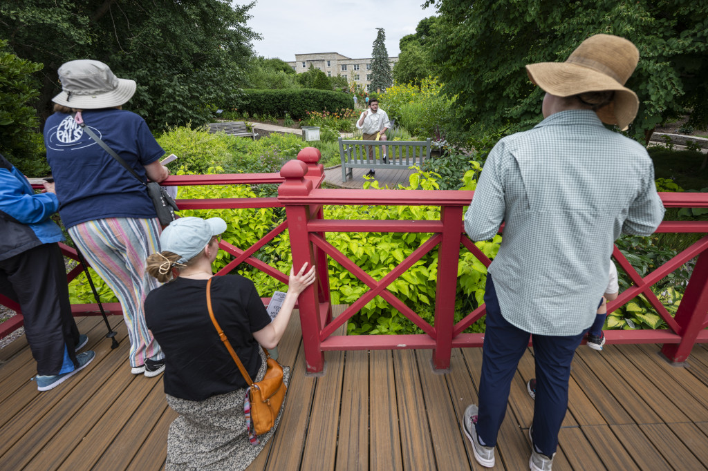 Two people watch a performance from a ridge over a small pond.