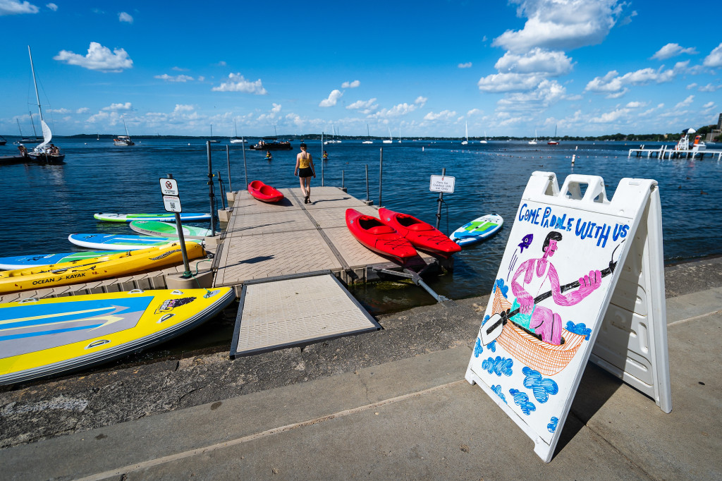 A number of kayaks are piled up on a dock on a lake.