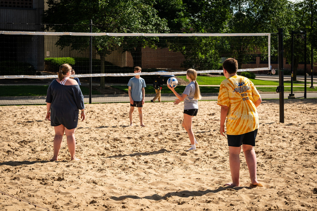A group of people play volleyball on a sand court.