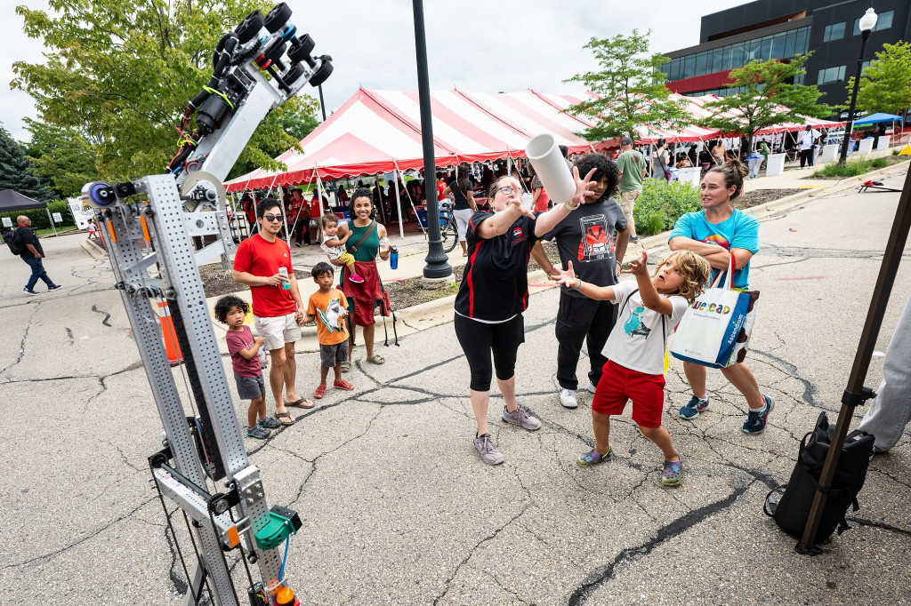 A group stands in front of a BadgerBot as they play a catch and toss game with the robot.