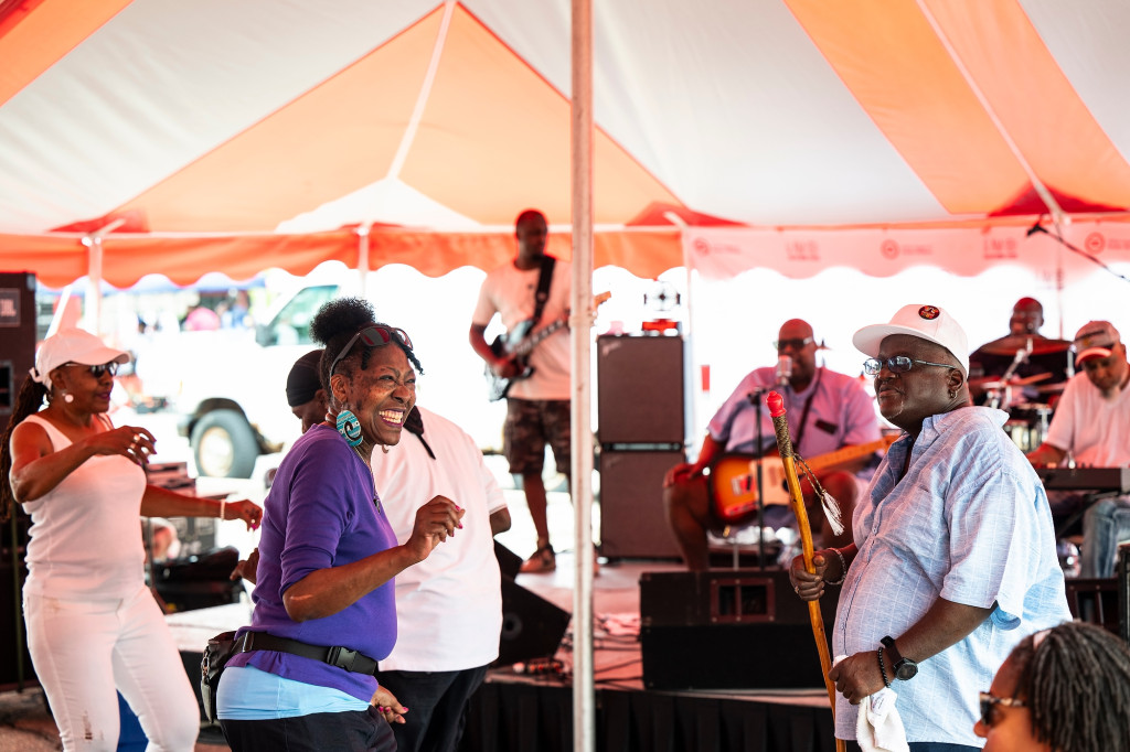 Event attendees dance to live music under a large red and white tent.