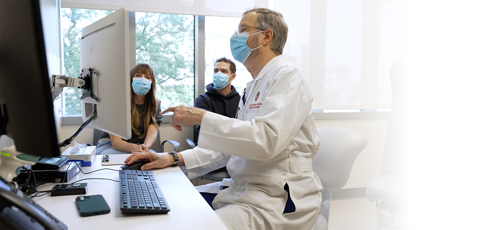 Doctor seated with two people at desk looking at computer screen.