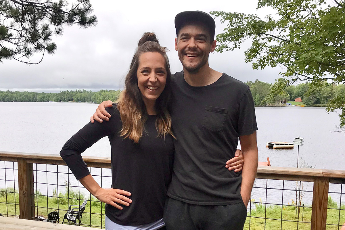 Meagan Hahn and Shawn Wiederhoeft, each with an arm around each other, smiling and standing on a deck with a lake behind them.