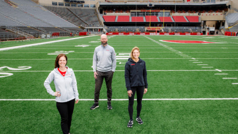 Maria Dehnert, Peter Miller, and Sara Jimenez Soffa stand at the 20 yard line in an empty Camp Randall stadium.