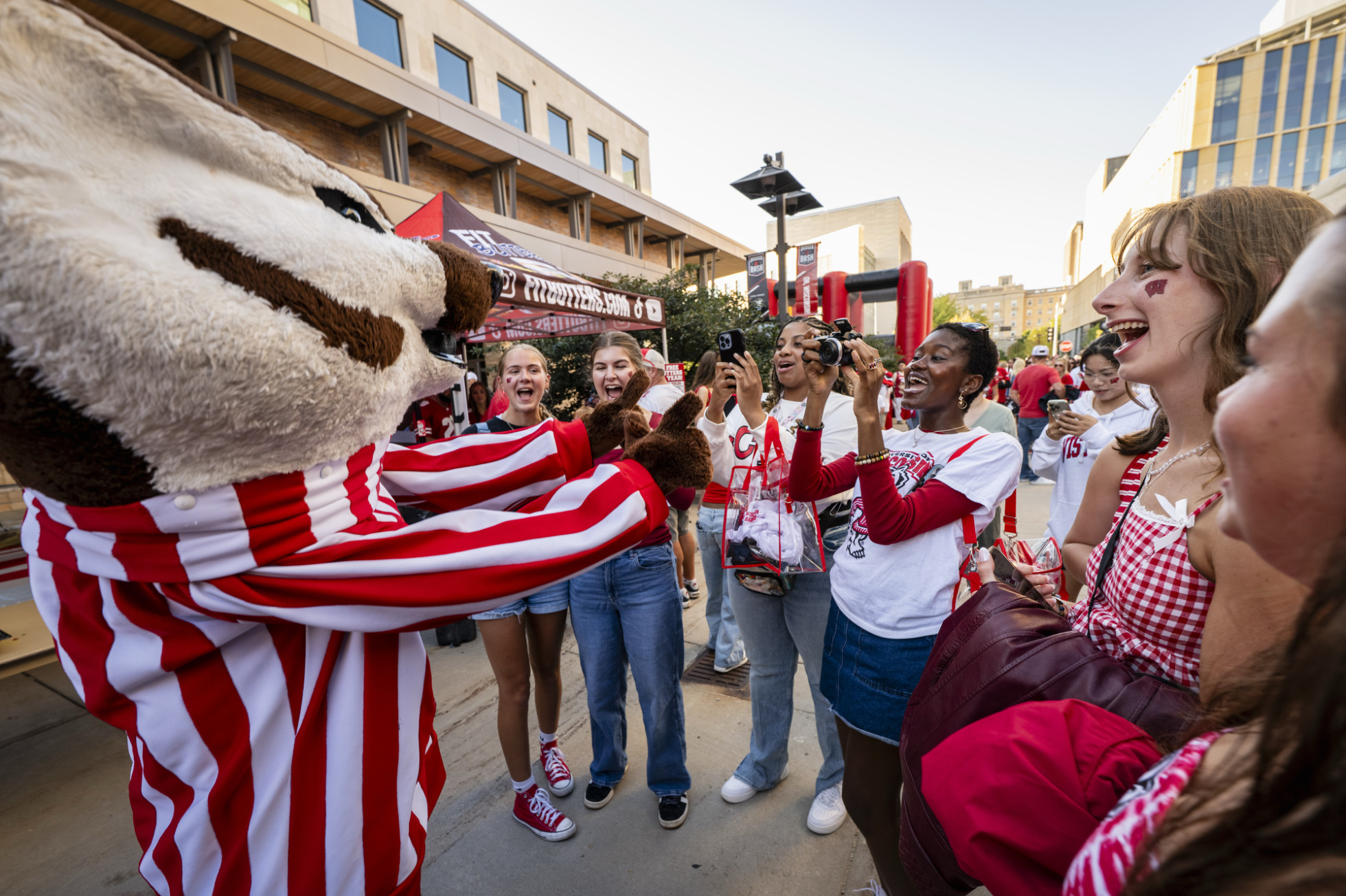 Smiling students take photos of Bucky Badger as he makes a W with his hand outside of Union South.