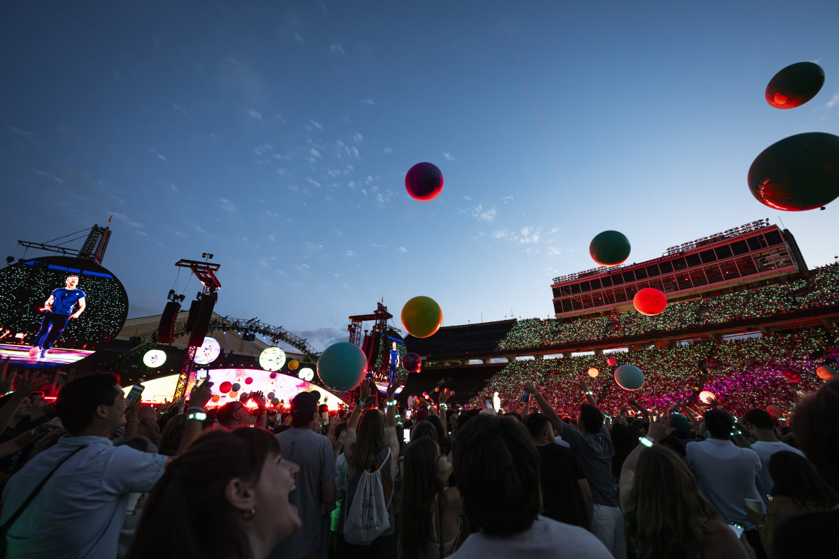 A packed stadium is shown with a stage all lit up and balloons rising above it.