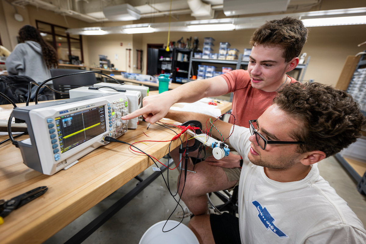 Two young men work on a piece of equipment with a screen.