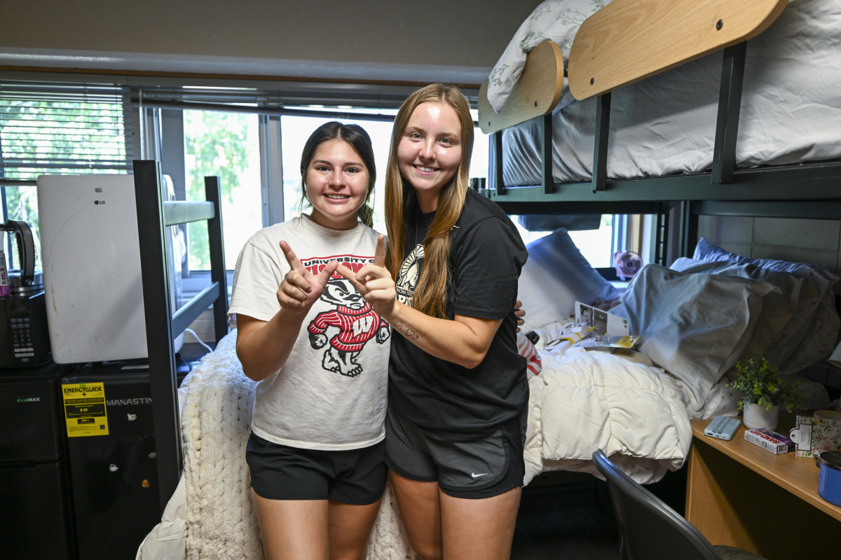 Inside their residence hall room, roommates Lillia Llontop and Sydney Stuntebeck make a W with their hands. 