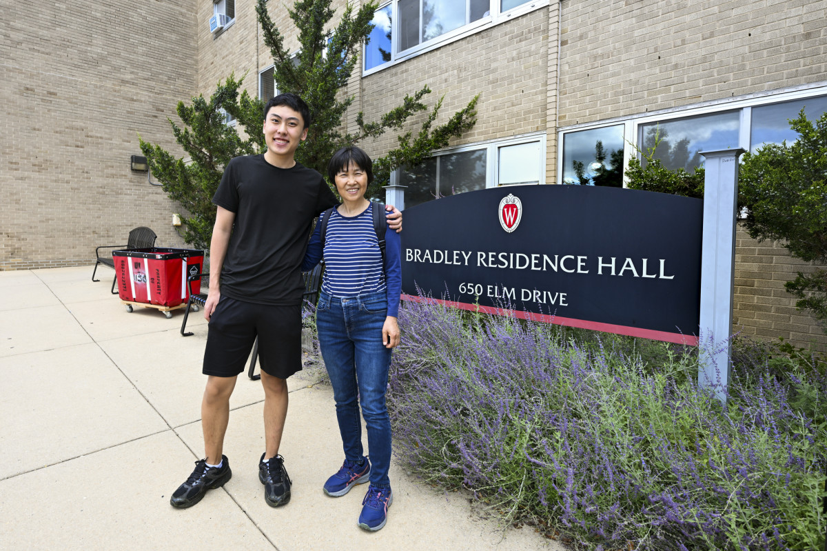 Josh Zhao poses arm in arm with his mom in front of a large Bradley Residence Hall sign.