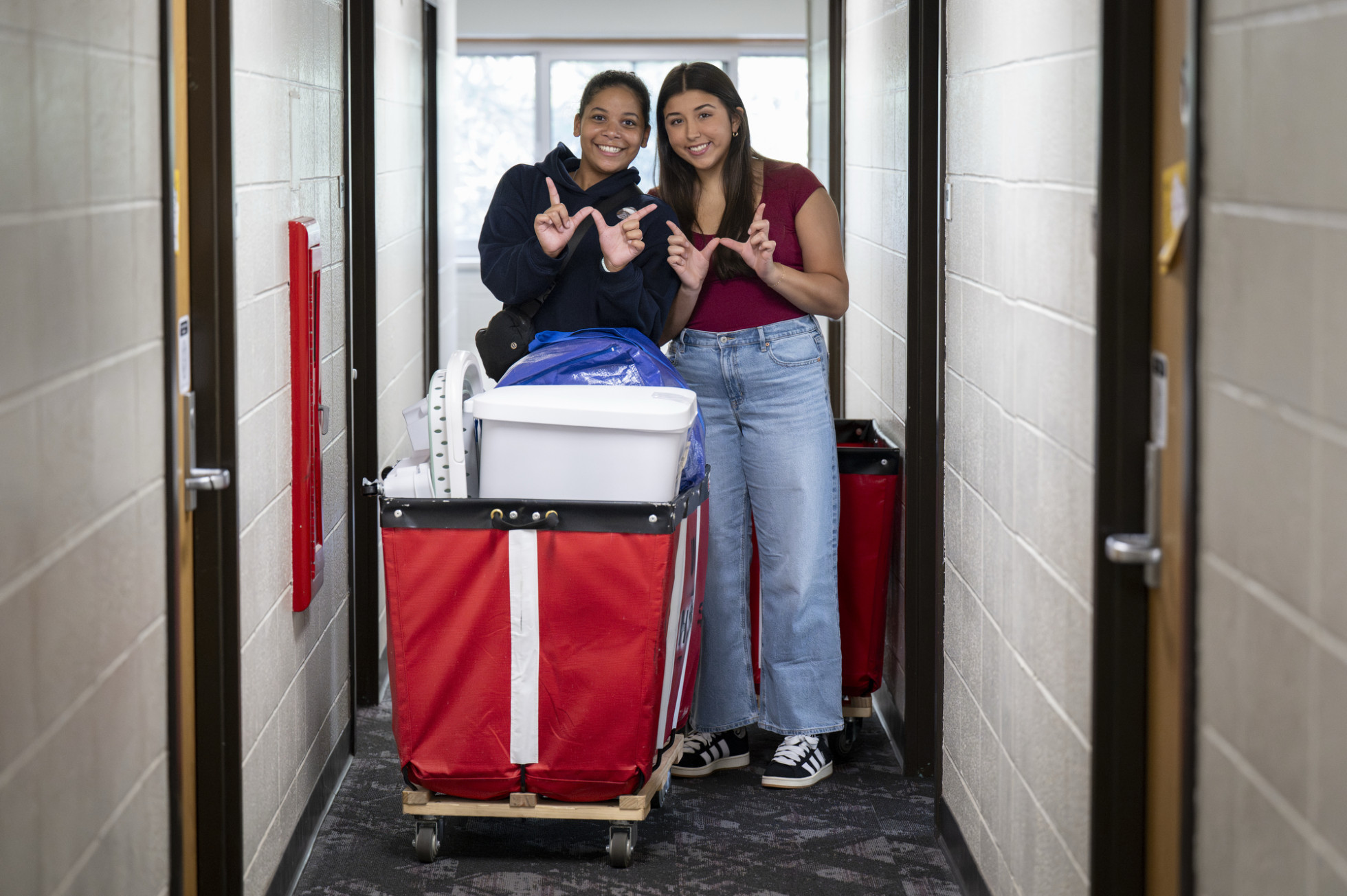 Roommates Leena Brown and Kaylee Katra make Ws with their hands, standing behind a moving cart.