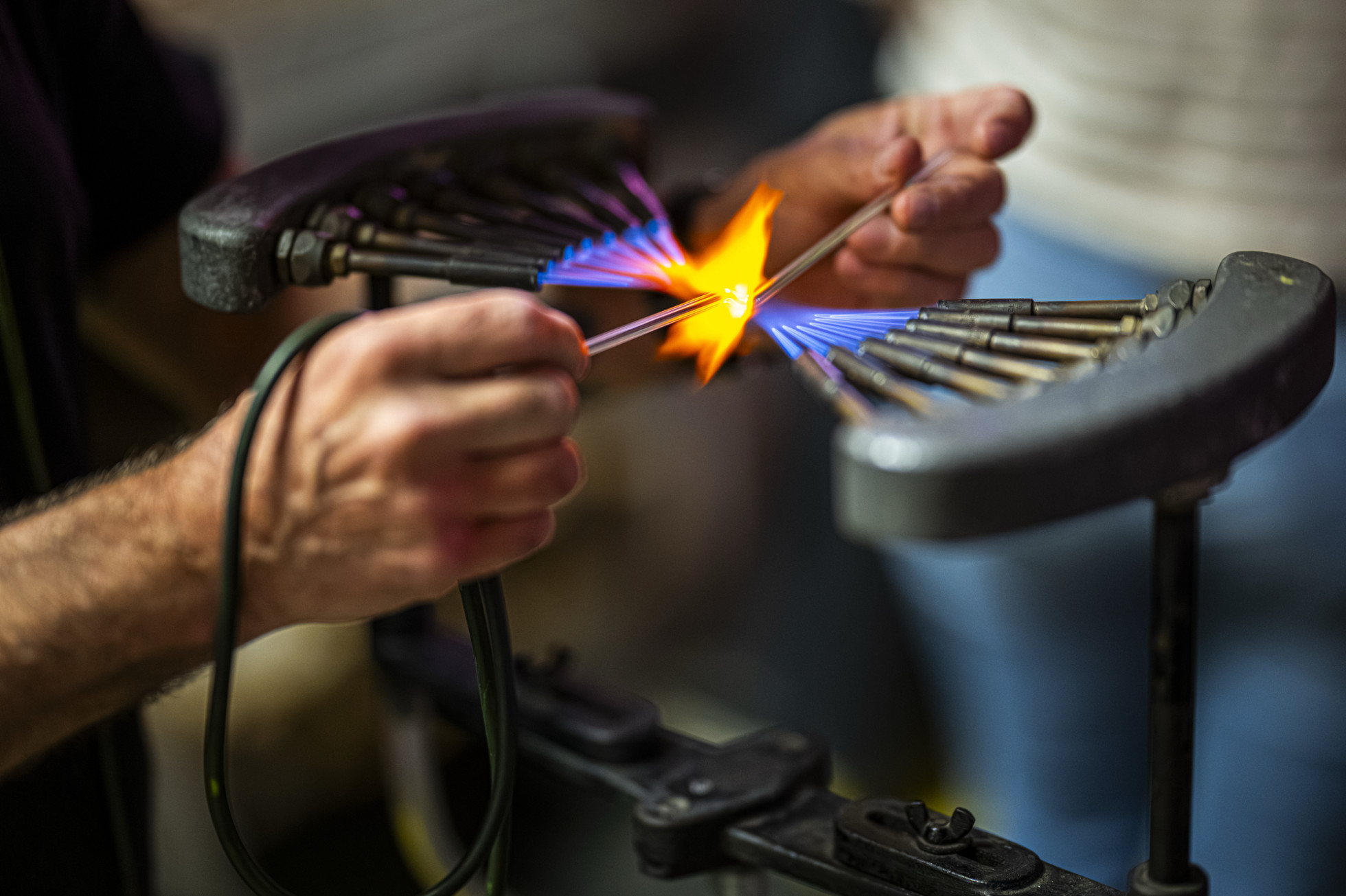 A close up of hands holding a glass tube over an open flame.