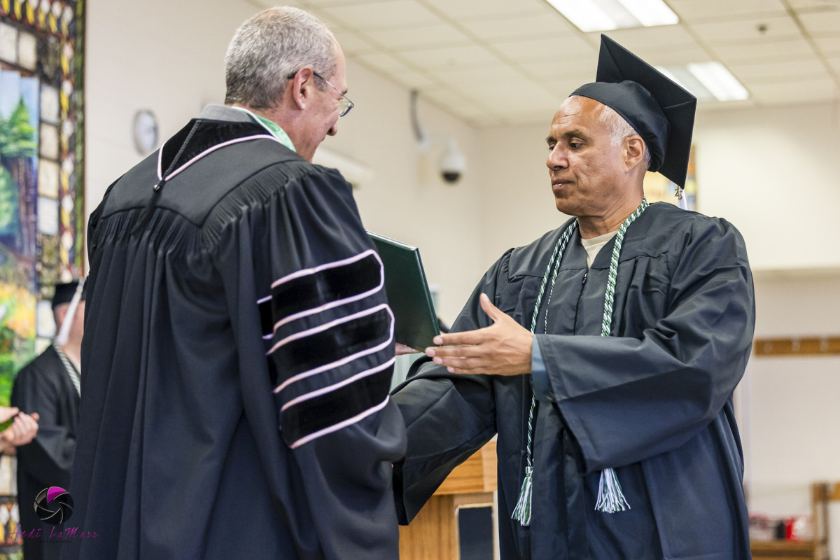 A photo of a man in a graduation robe and cap shaking the hand of another man in academic robes at a graduation ceremony.