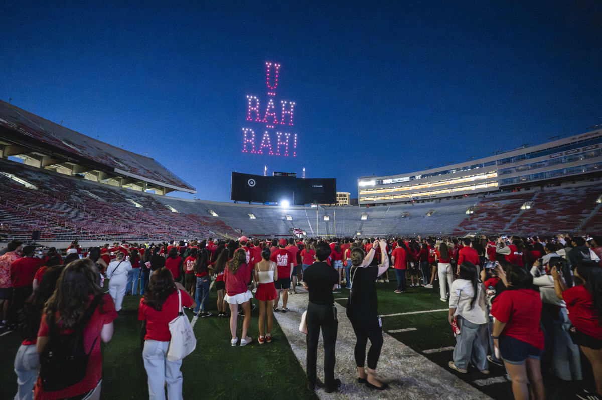 Drones in a darkened sky  form the words U Rah Rah as people watch from a football stadium.