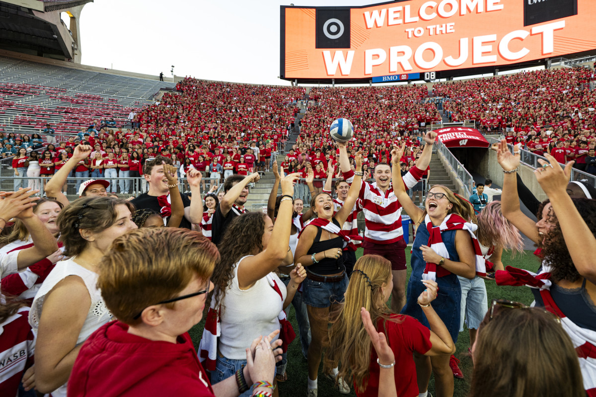 People wearing red and white cheer in a football stadium stands.
