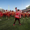 The mascot Bucky Badger holds up his fist and cheers as he's surrounded by cheerleader.