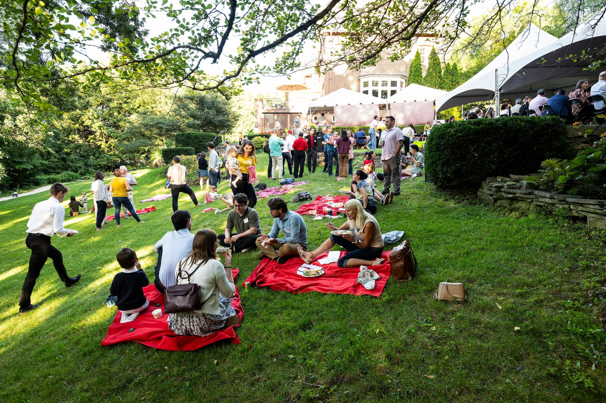 Picnic blankets dot the Olin House backyard. Some hold people who enjoy their meals while more picnic attendees mull around the grounds.