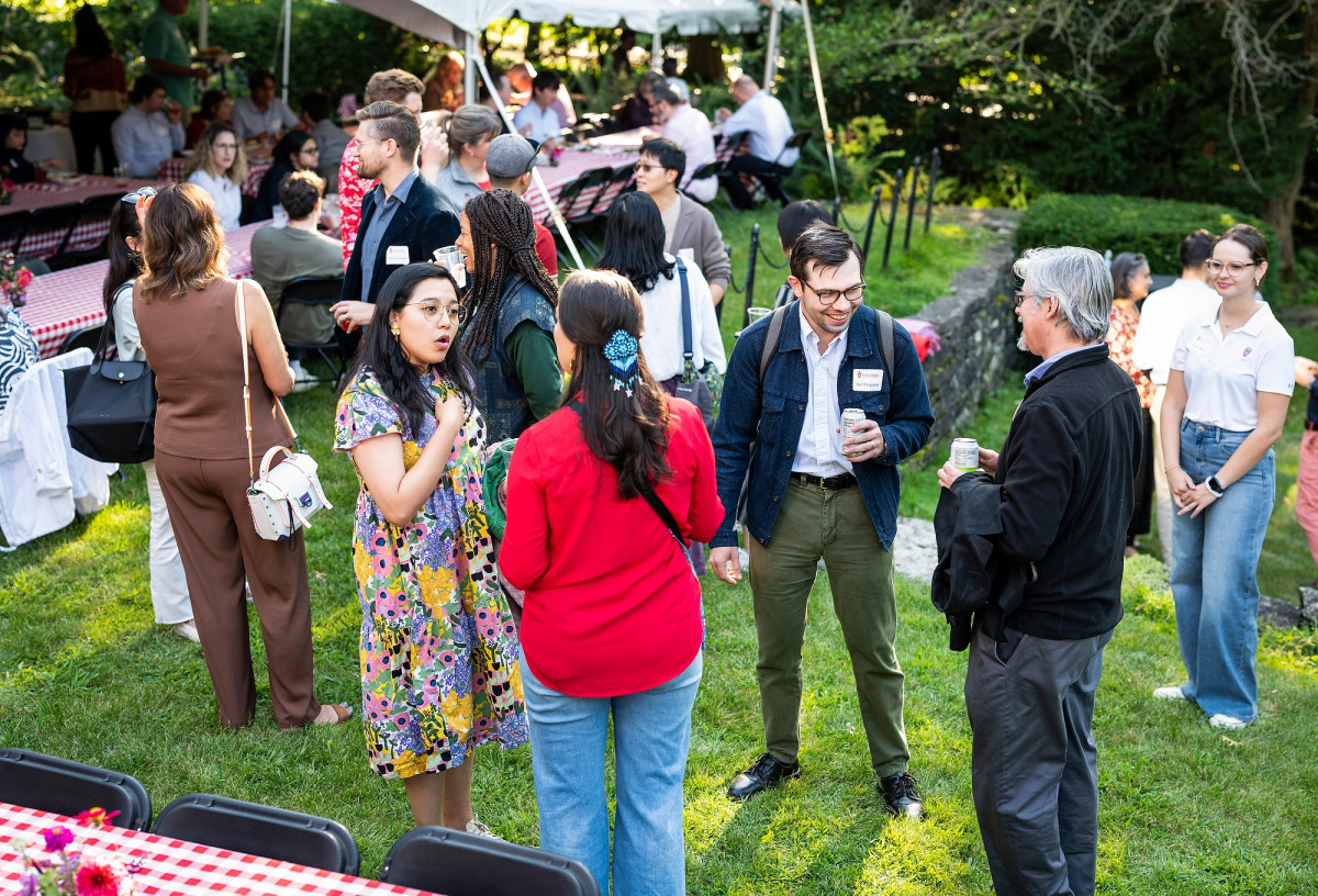 A group of new faculty dot the backyard of Olin House. Some pairs stand in conversation with one another while others address groups of fellow faculty.