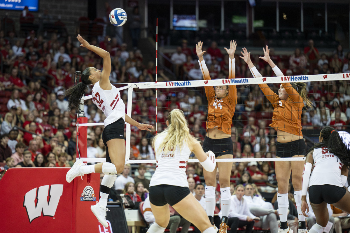 Egan, in mid jump, spikes the ball across from two Texas Longhorn players who are jumping up in an attempt to stop the ball.