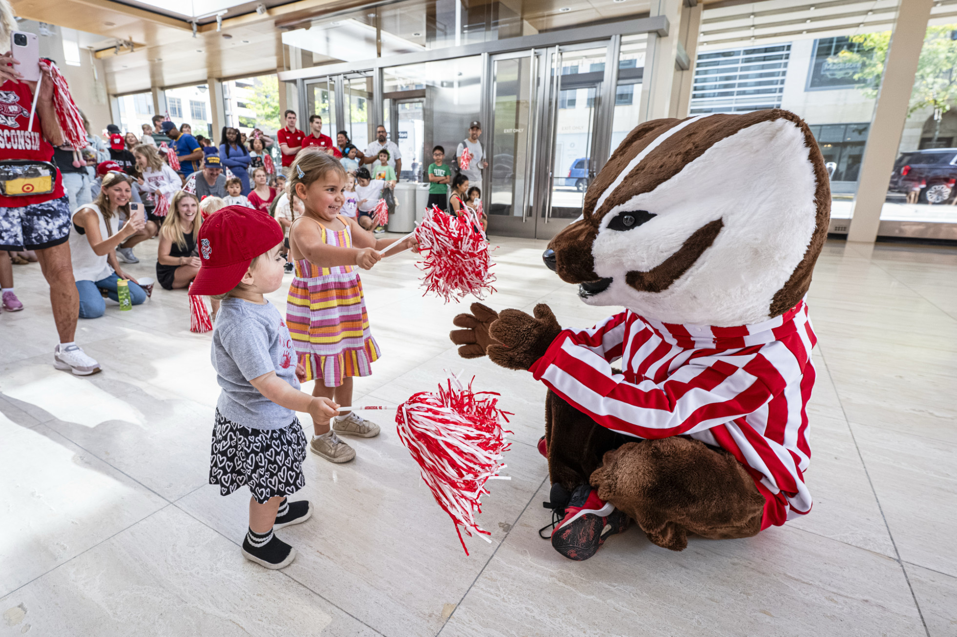 Bucky sits on the floor to interact with two children in the Overture Center atrium. 