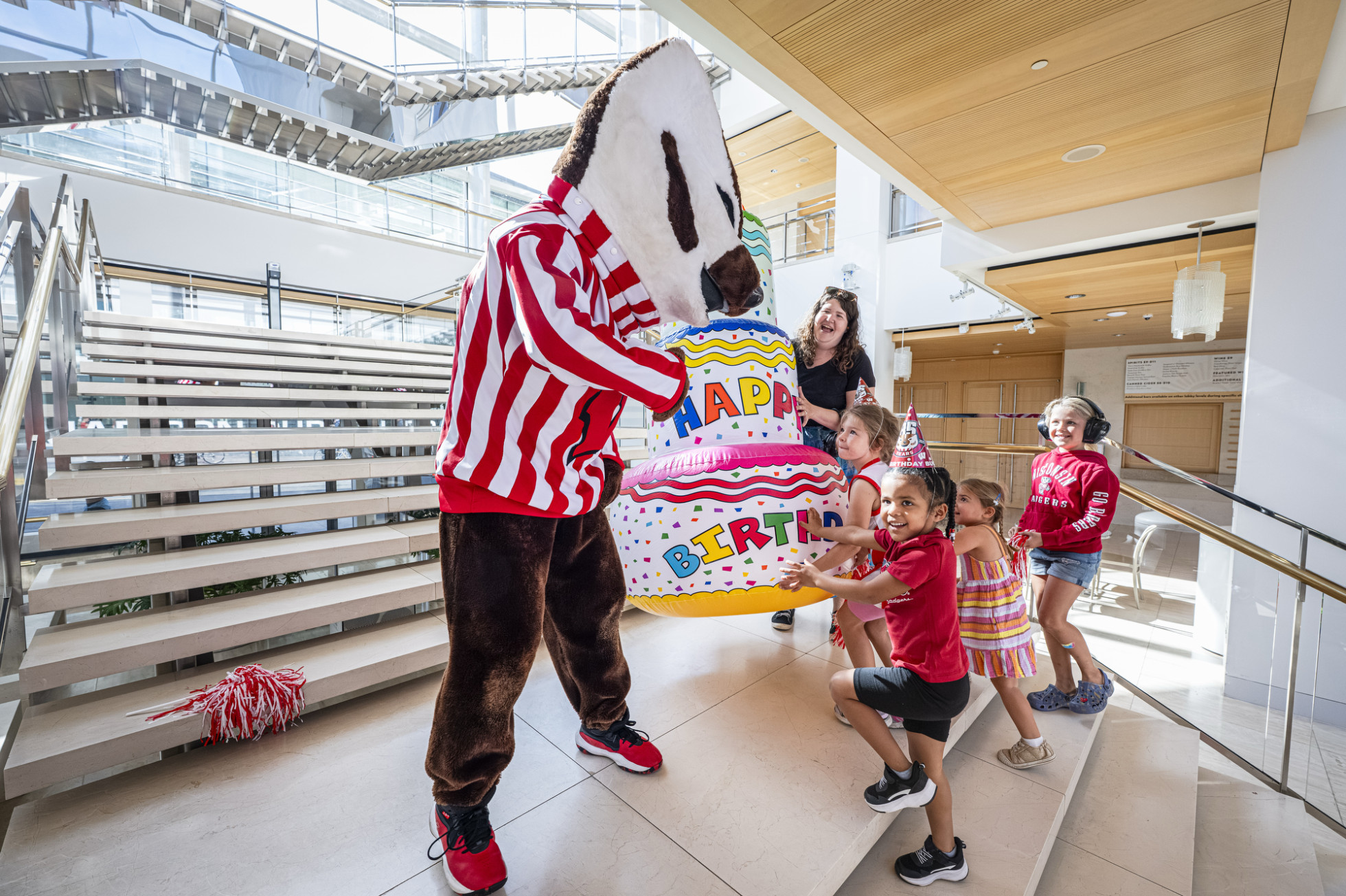 Bucky Badger accepts an inflatable birthday cake from a group of children inside the Overture Center. 
