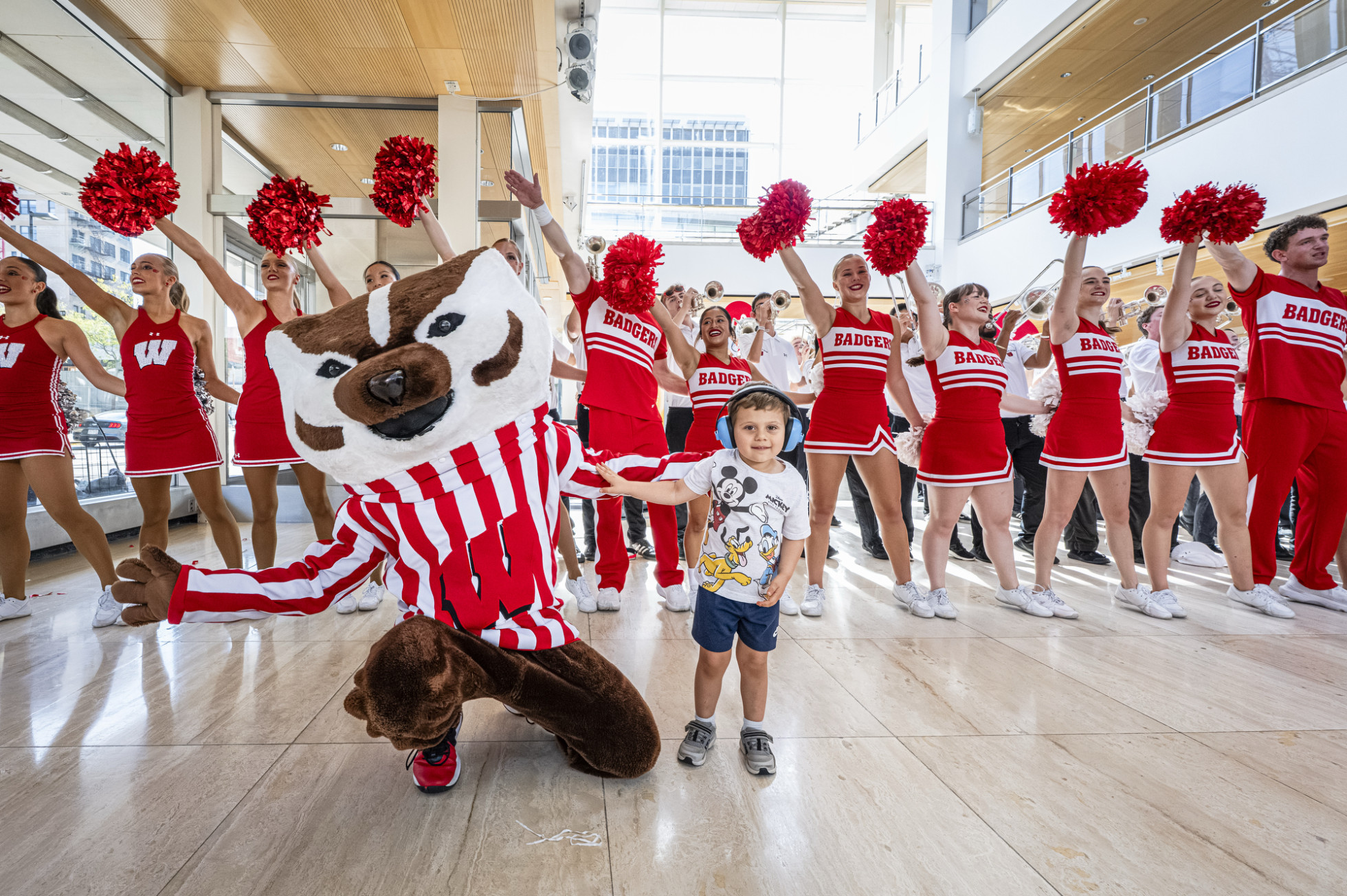 With arms open, Bucky Badger poses with a child in front of the UW Spirit Squad inside the Overture Center.
