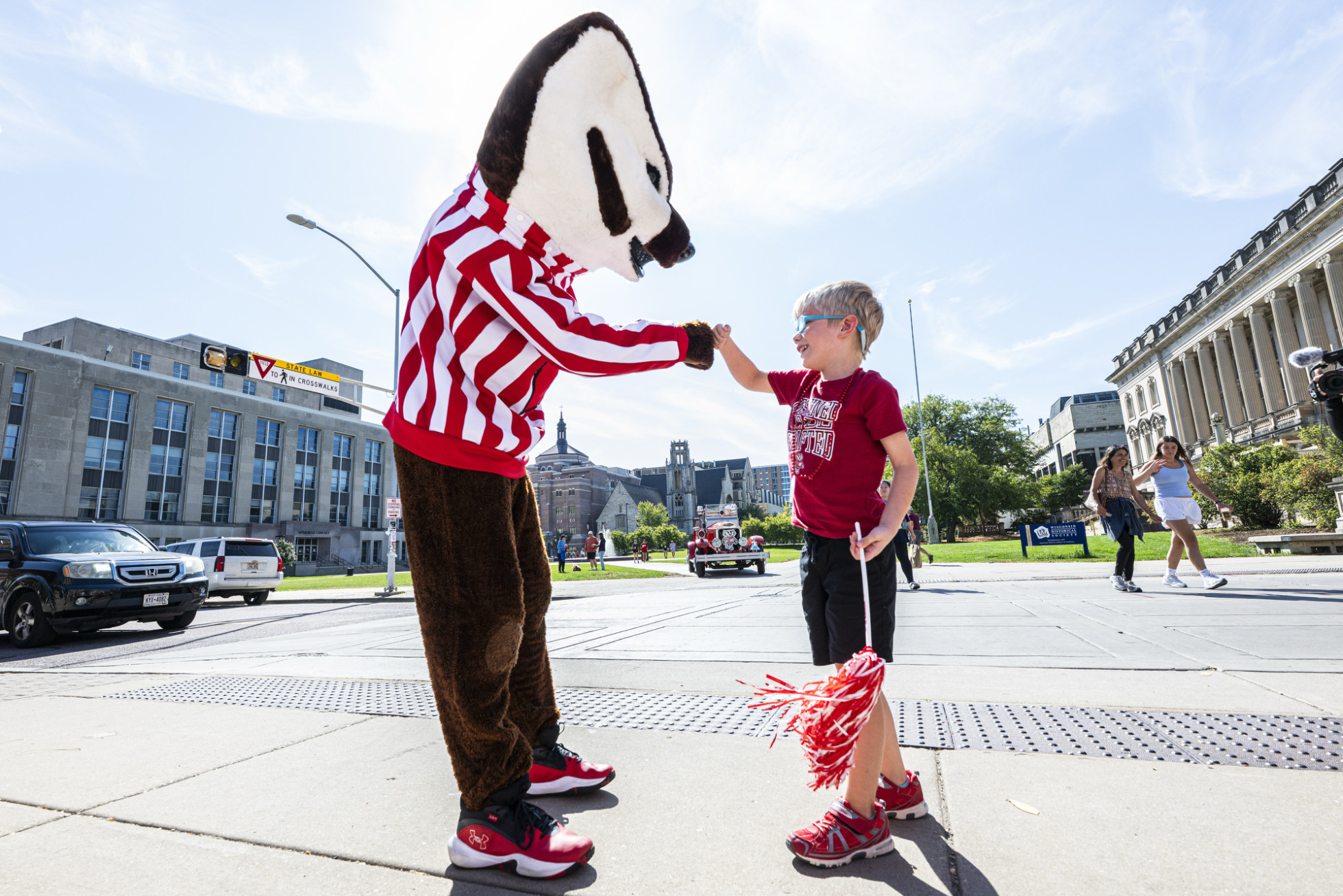 Bucky fist bumps with a child in front of the Memorial Union Terrace.