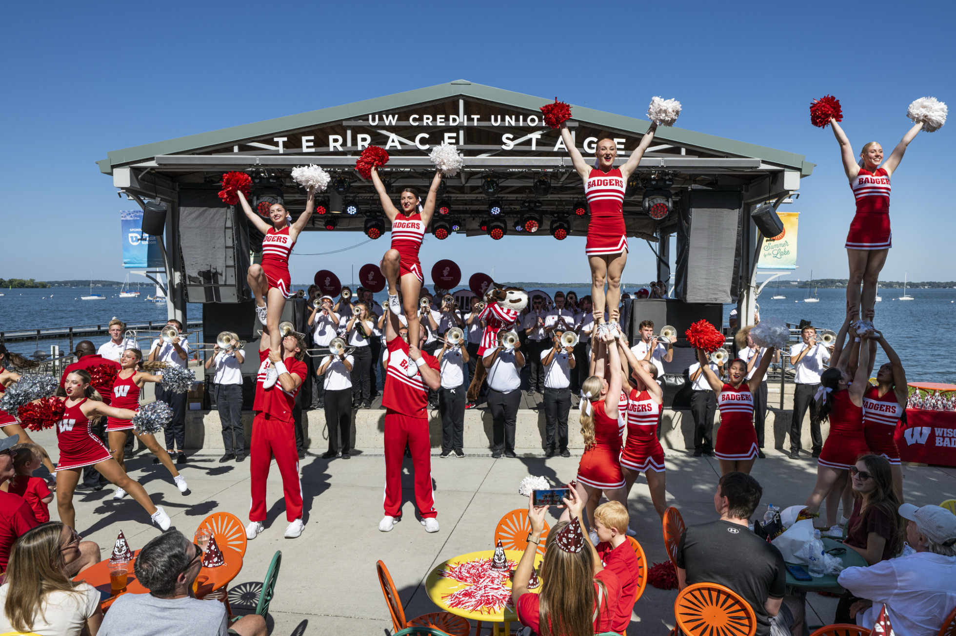 The UW Spirit Squad cheerleaders and the UW Marching Band play on the Memorial Union Terrace in front of the lake.