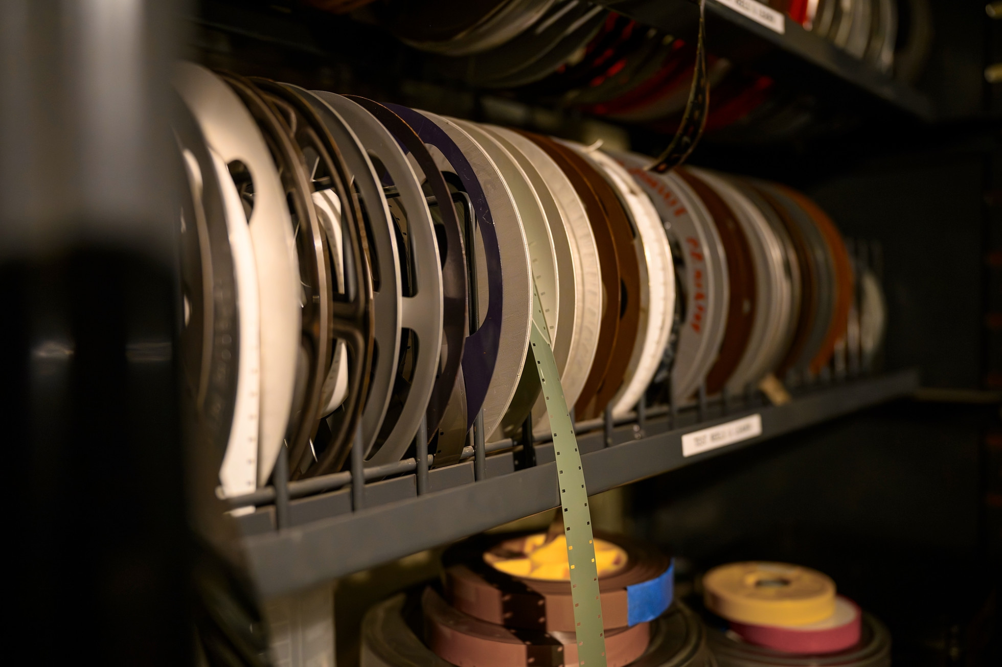 A shelf filled with colorful archival film reels, some with hanging strips.