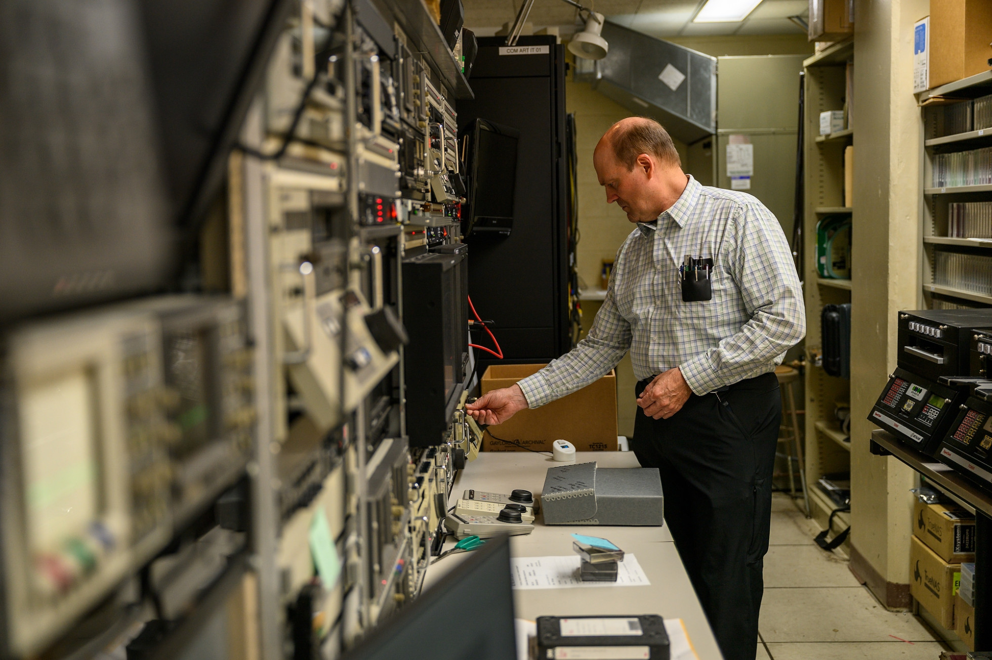 Boyd Hillestad adjusts equipment in a room filled with electronic devices and shelves.