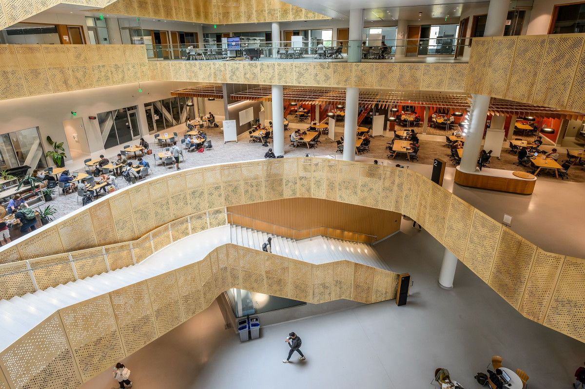 A view of the atrium of Morgridge Hall features bright nature light and a large, circular staircase, with students dotting every floor. 