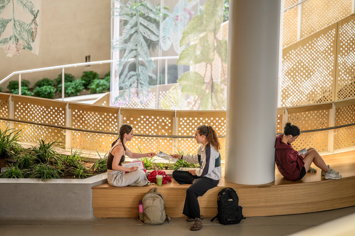 Two students sit in conversation on a sunlit bench in the atrium of Morgridge Hall.