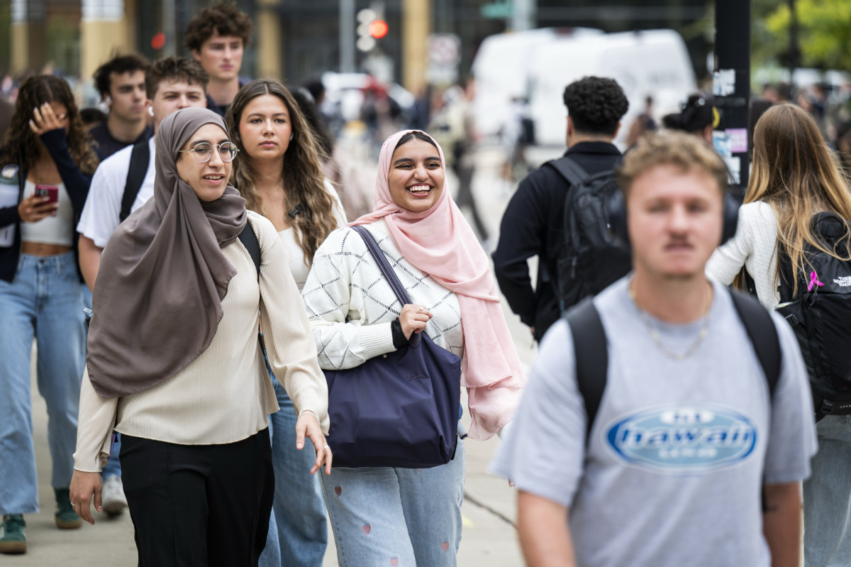 Two women laugh and talk as they walk in a crowd on their way to class.