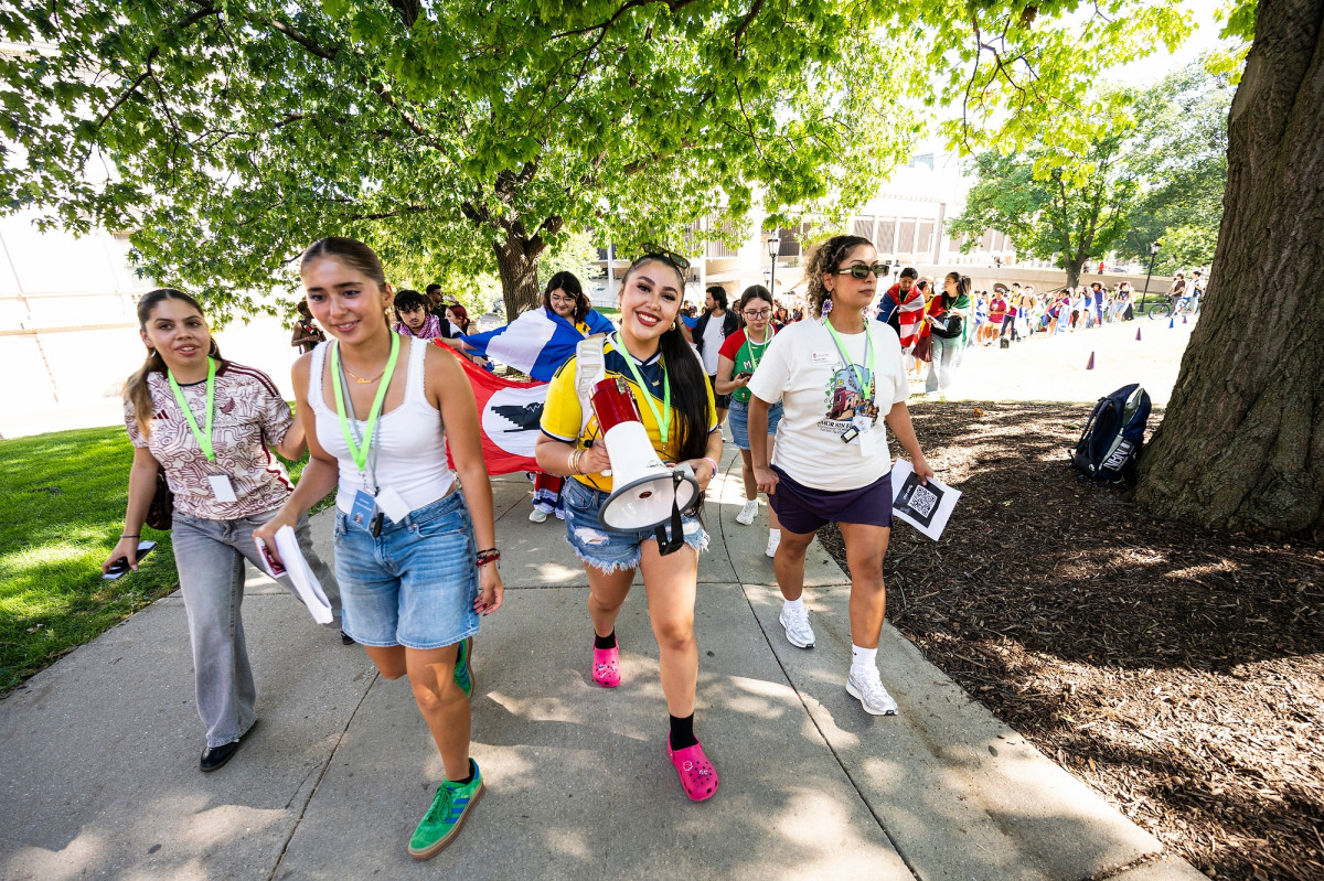 A long procession of students carrying national flags smile and celebrate as they walk up Bascom Hill.