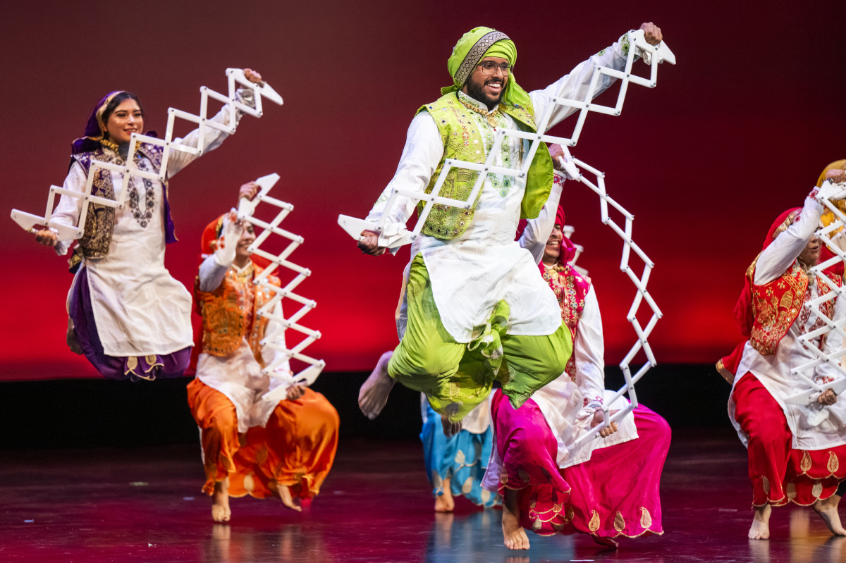 A group of students wearing cultural attire from the Punjab region of India dance to a song while holding fans in their hands. 