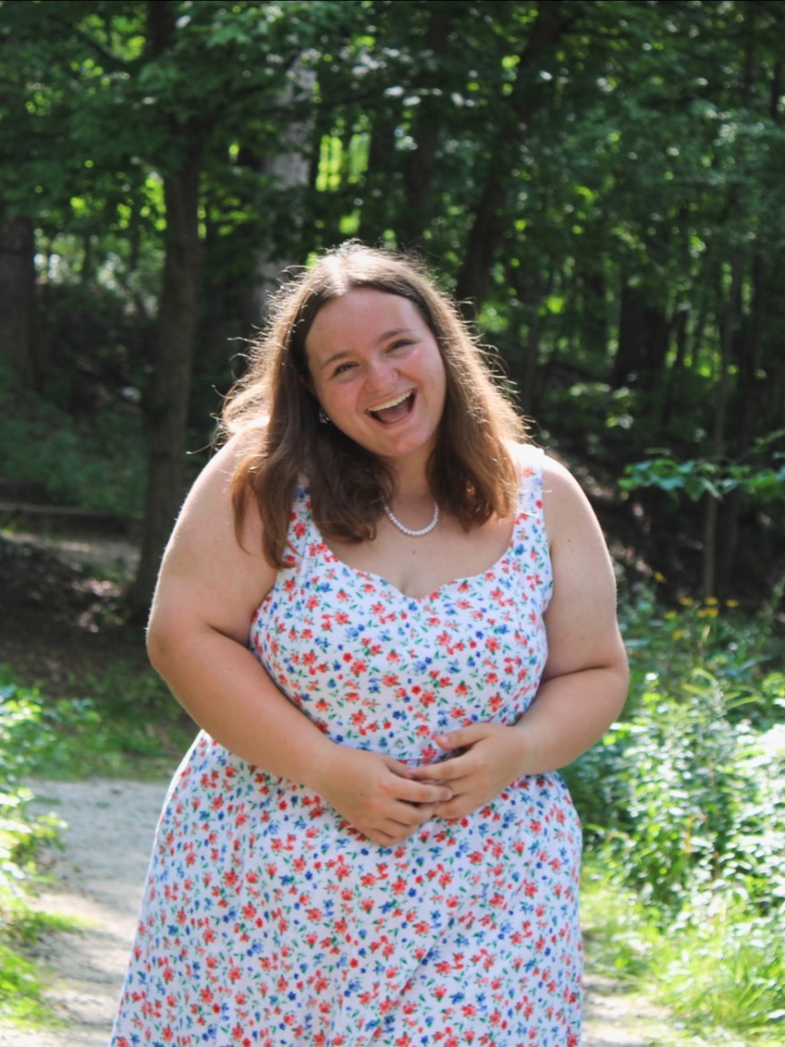 Mercier smiles for a portrait photo in front of summer foliage.