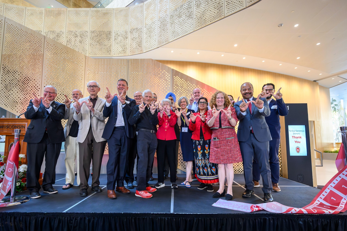 A group of people stand on stage and hold up 'W' signs with their hands.