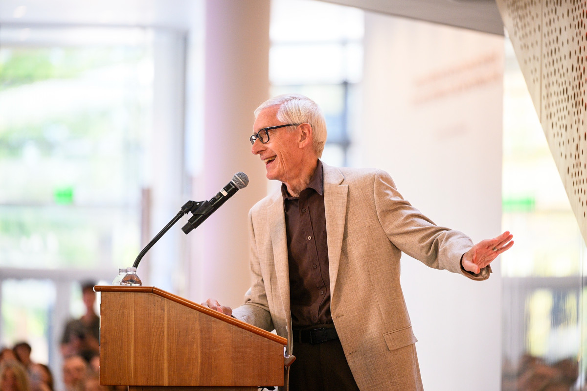 Evers stands behind the podium and speaks into the microphone as he points to something on stage.